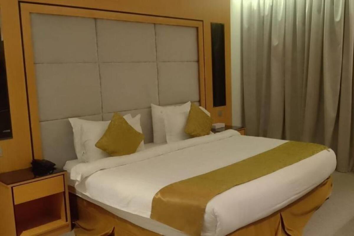 A hotel room with a large bed, a nightstand, a chair, and a window with curtains.