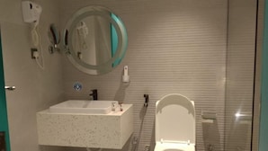 Une salle de bain avec des toilettes blanches, un lavabo, un miroir et une douchette à main.