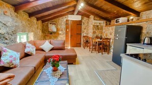 Ein gemütliches Zimmer mit Steinwand, Holzboden, einer Couch, einem Esstisch mit Stühlen und einer Küchenzeile mit Kühlschrank.
