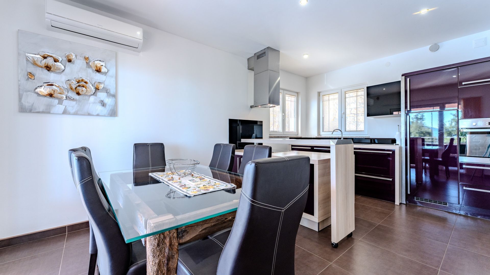 A modern kitchen with a dining area, featuring a glass table, black chairs, and a TV.
