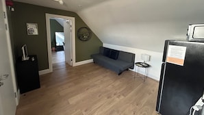 A room with a wooden floor, a gray sofa, a black refrigerator, and a door leading to another room. - Dublin citycenter 1 bedroom Apartment (Dublin)