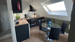 A compact kitchen with a skylight, a dining area with a glass table and black chairs, and a small potted plant. - Dublin citycenter 1 bedroom Apartment (Dublin)