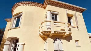 A two-story building with a curved facade, a balcony with a white balustrade, and a tiled roof. - JF IMMO-VILLA RARE GARDEN PRIVATE POOL 10 PEOPLE SEA VIEW V0861 (Agde)