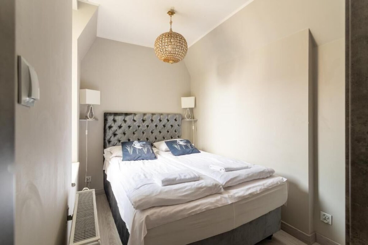 A bedroom with a tufted headboard, two bedside lamps, a bed with white linens, and a hanging light fixture.