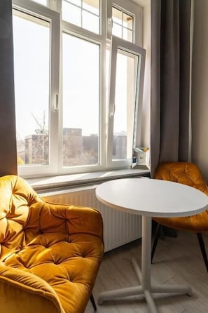 Une pièce avec une grande fenêtre, une table blanche et deux chaises jaunes.