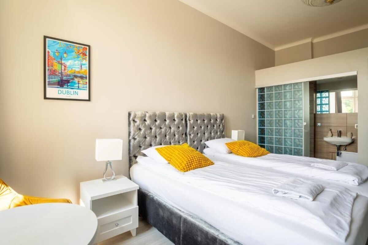 A hotel room with a bed, a nightstand, a chair, a painting, and a bathroom with a sink.
