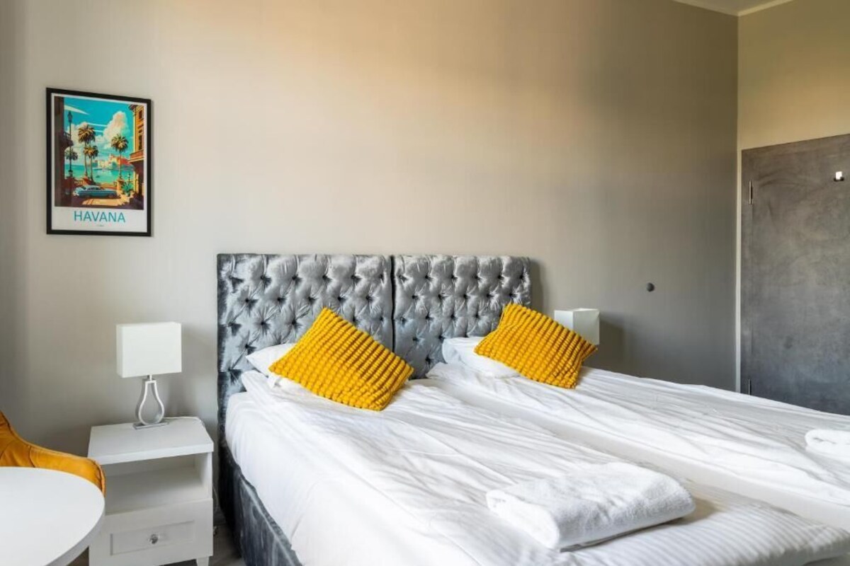 A hotel room with a large bed, two bedside tables, a nightstand, and a wall-mounted lamp.