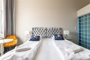 A hotel room with a large bed, two bedside tables with lamps, a small round table, a yellow chair, and a view of the city.