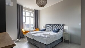 A double bed with a tufted headboard, a bedside table with a lamp, a chair, and a window with curtains. - Imperial Apartments - GlobElite Sopot (Sopot)