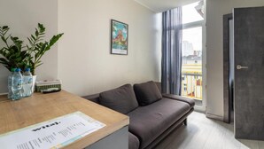 A modern room with a sofa, a wooden table with a document, a potted plant, and a window with curtains. - Imperial Apartments - GlobElite Sopot (Sopot)