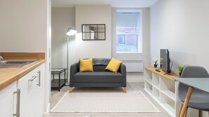 Una sala de estar moderna con un sofá gris, una mesita de madera y un escritorio con una computadora.