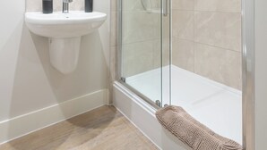Un baño moderno con ducha envuelta en vidrio, un lavamanos blanco y un espejo.