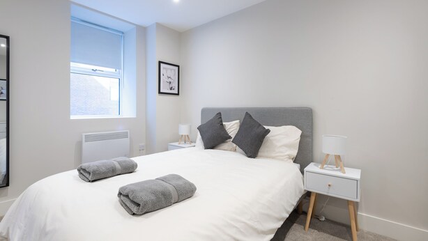 Un dormitorio moderno con una cama grande, dos mesitas de noche, una ventana y un cuadro colgado en la pared.