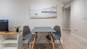 Una habitación moderna con un escritorio, dos sillas, un cuadro de una escena costera y un televisor.