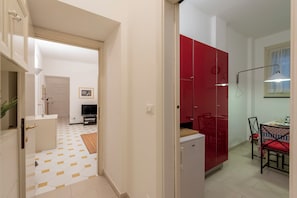 Un pasillo con piso estampado, un armario rojo, un refrigerador pequeño y un comedor con sillas y una mesa.