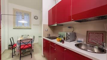 Una cucina compatta con mobili rossi, un piano di lavoro bianco, un lavandino in acciaio inox, un tostapane e una finestra con tende.