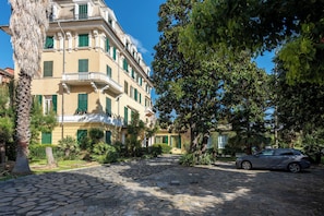 Una calle adoquinada que conduce a un edificio de varios pisos con balcones y contraventanas verdes.