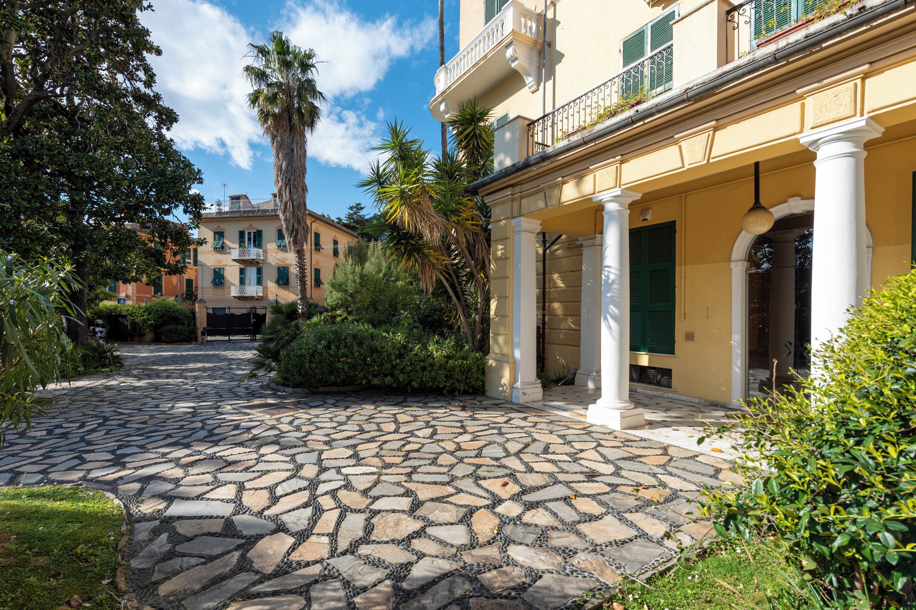 Un cortile con pavimento in pietra, un edificio con colonne e una palma.