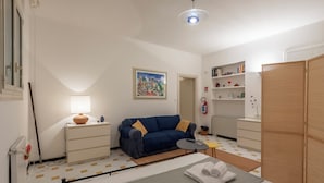 Ein Zimmer mit einem Bett, einer Couch, einem kleinen Tisch, einer Lampe, einem Gemälde, einem Bücherregal und einem Kleiderschrank.