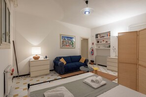 Ein Zimmer mit einem Bett, einer Couch, einem kleinen Tisch, einer Lampe, einem Gemälde, einem Bücherregal und einem Kleiderschrank.