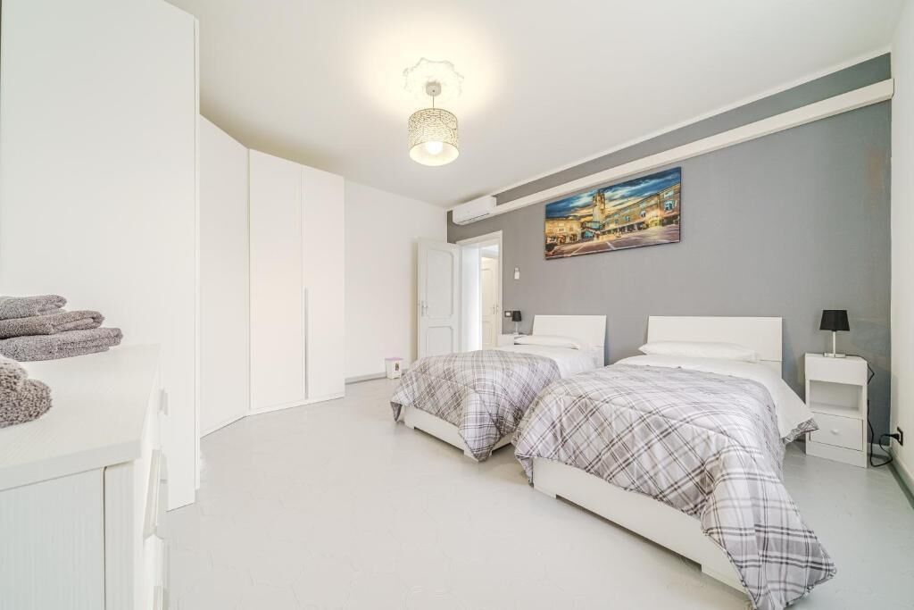 Une chambre avec deux lits, un tableau au mur et un luminaire au plafond.