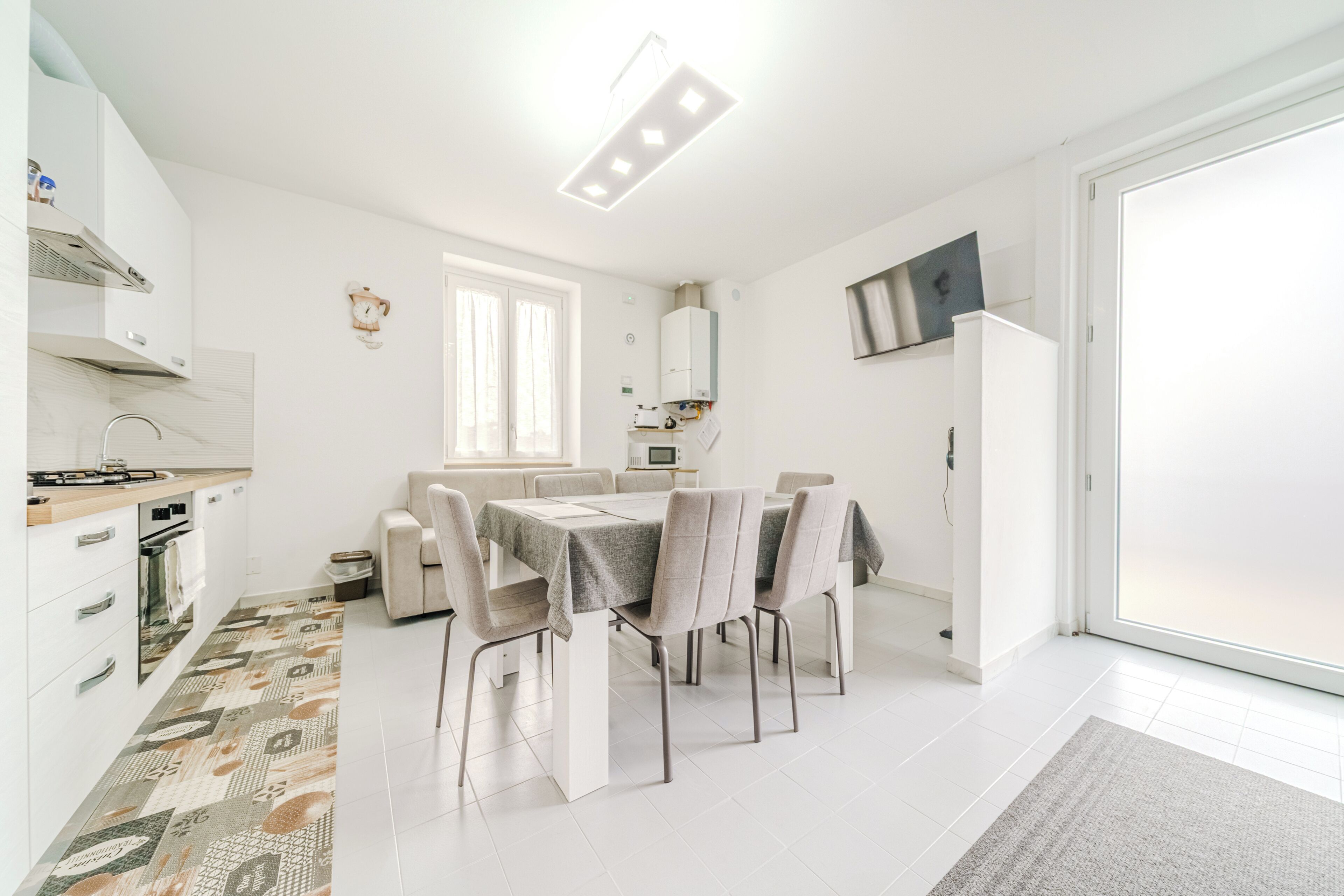 A modern kitchen with white cabinets, a dining area with a table and chairs, and a large window.