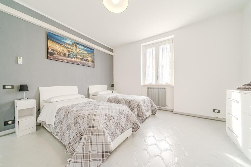 Een slaapkamer met twee bedden, een nachtkastje, een dressoir, een schilderij en een raam.