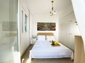 A bedroom with a bed, a nightstand, a painting, and a wardrobe. - Salty Olive Cabana by RentalsPro - Akti Salonikiou (Salonikiou)