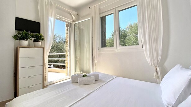 Un dormitorio con cama, televisor, cómoda y ventana con cortinas.