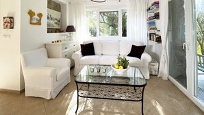 Una sala de estar con un sofá blanco, una mesa de centro de vidrio y una estantería.