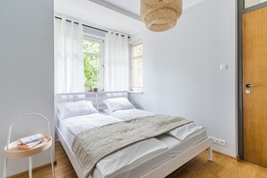 A bedroom with a bed, two windows with curtains, a bedside table with a lamp, and a wooden door. - Imperial Apartments - Nadmorski Zen (Sopot)