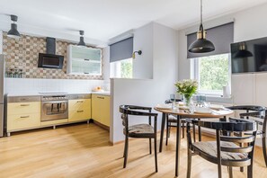 A modern kitchen with a built-in oven, a dining area with a round table and chairs, and a large window providing natural light. - Imperial Apartments - Nadmorski Zen (Sopot)