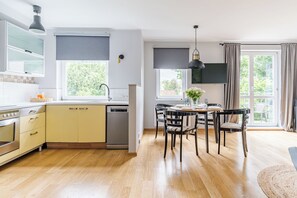A modern kitchen with a dining area, wooden flooring, and large windows.