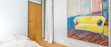 Un dormitorio con cama, una puerta, un cuadro y un ventilador de techo.