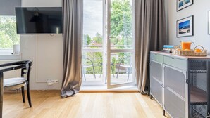 Une chambre dotée d’une télévision, d’une table à manger, d’une chaise, d’un balcon avec des rideaux et d’une kitchenette équipée d’un réfrigérateur.