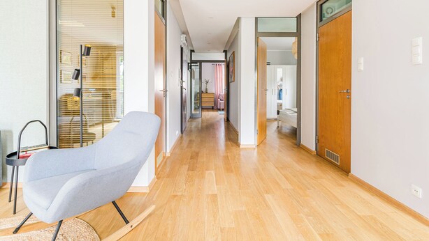 Un intérieur moderne avec un plancher en bois, un fauteuil de couleur grise et une porte en verre donnant sur une salle de bain.
