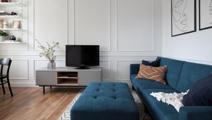 Ein modernes Wohnzimmer mit einem Flachbildfernseher, einem blauen Sofa und einem weißen Konsolentisch.