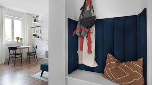 Ein Zimmer mit einer blauen gepolsterten Bank, einer hängenden Tasche und einem weißen Regal mit Gegenständen.