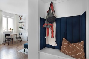 A room with a blue padded bench, a hanging bag, and a white shelf with items. - Imperial Apartments - Zatoka (Sopot)