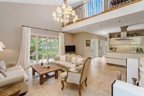 A spacious living area with a sofa, coffee table, and a chair, a kitchen with cabinets and a TV, and a balcony with curtains. - Villa with Pool, Vineyard and Sea Views in La Croix-Valmer (La Croix-Valmer)