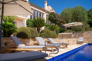 Un espace aménagé au bord de la piscine, avec des chaises longues, des parasols et un mur en pierre.