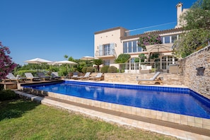 A swimming pool with lounge chairs, a stone wall, and a building with balconies. - Villa with Pool, Vineyard and Sea Views in La Croix-Valmer (La Croix-Valmer)