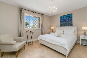 A bedroom with a bed, a chair, a window with curtains, a chandelier, and a painting on the wall. - Villa with Pool, Vineyard and Sea Views in La Croix-Valmer (La Croix-Valmer)