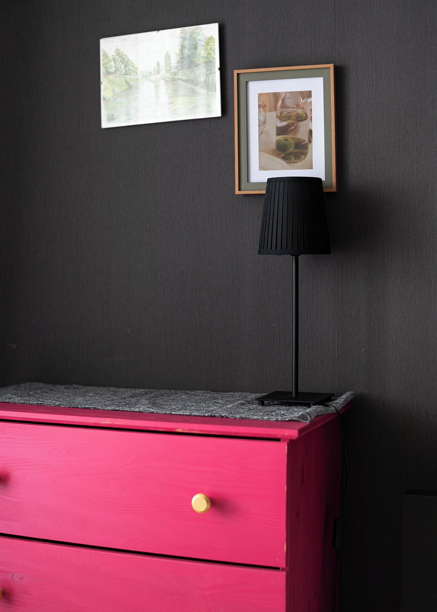 A red dresser with a drawer, a black lamp, and two framed pictures on a dark wall.