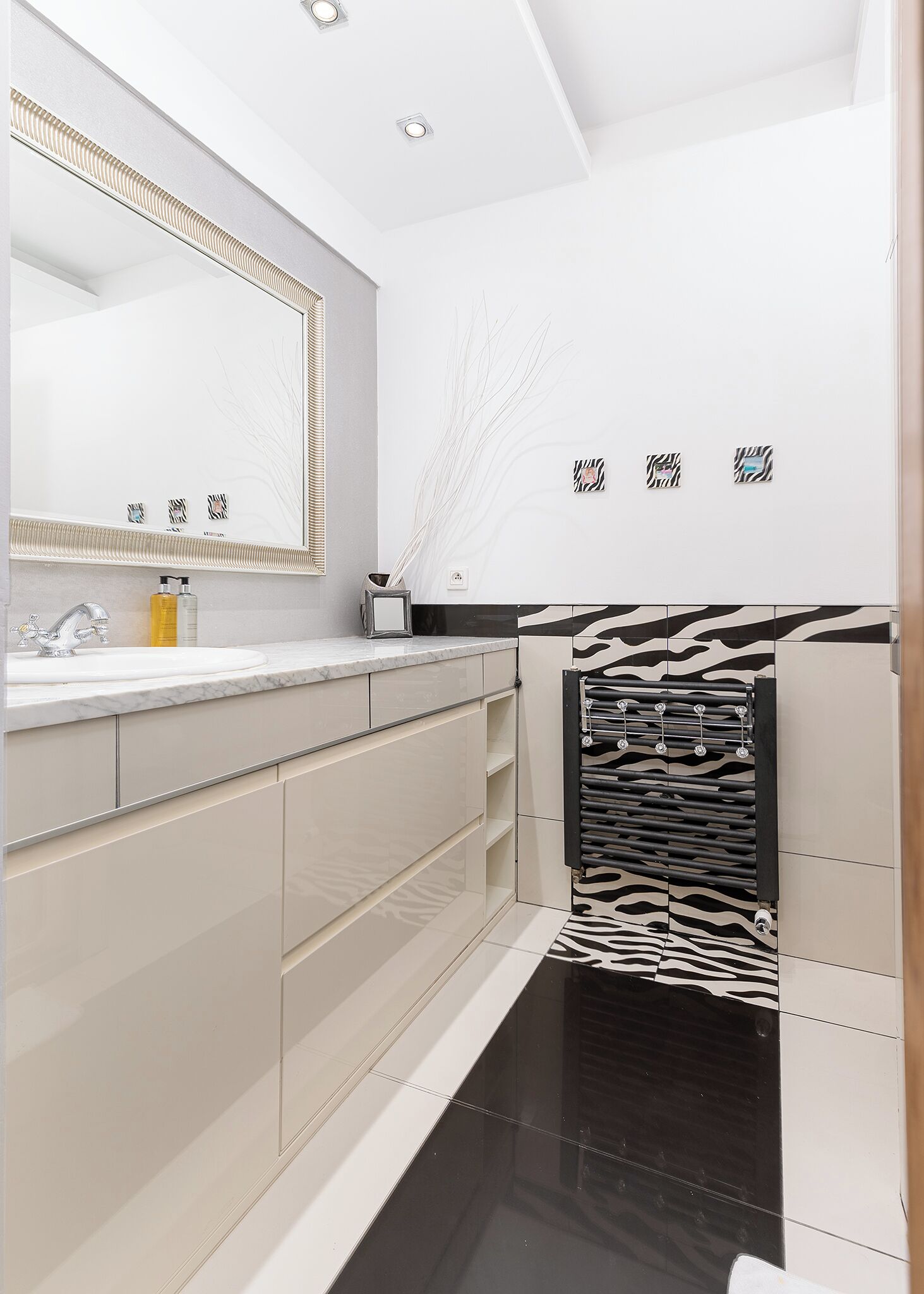 Un baño moderno con un espejo grande, un lavabo redondo y una cabina de ducha con estampado de cebra.