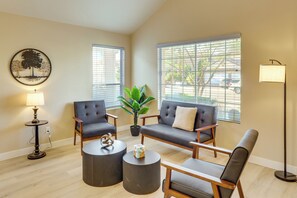 A living room with a sofa, two armchairs, a coffee table, a floor lamp, a potted plant, and a wall art piece.