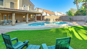 Un patio trasero con piscina, mobiliario de exterior y césped cuidado.