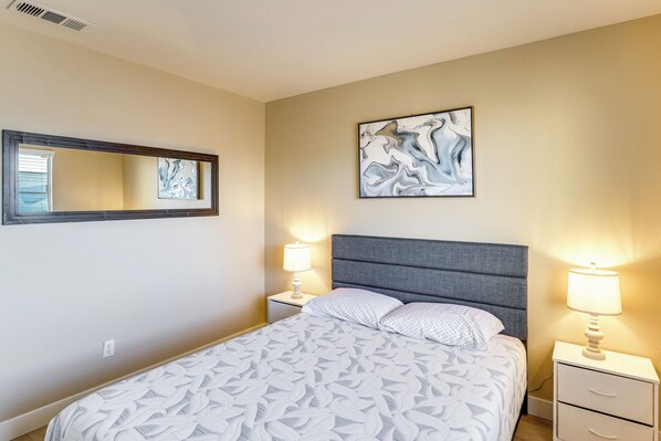A bedroom with a bed, two bedside tables, a nightstand, a wall-mounted mirror, and two wall-mounted lamps.