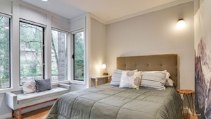 A bedroom with a large bed, a bench by the window, and a view of trees. - Relax Poolside! All-season Base in Mt Hood Village (Welches)
