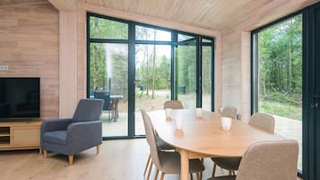 A modern interior with a wooden ceiling, a TV, a dining table with chairs, and large glass doors leading to an outdoor area.